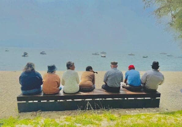 Um grupo de seniores sentados num banco, de frente para a água